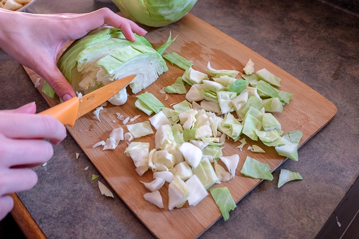green cabbage being diced on wooden cutting board