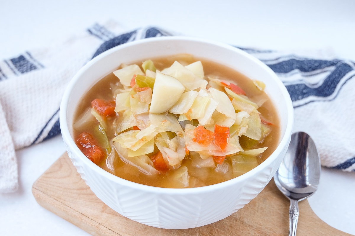 bowl of cabbage potato soup on wooden board with silver spoon beside