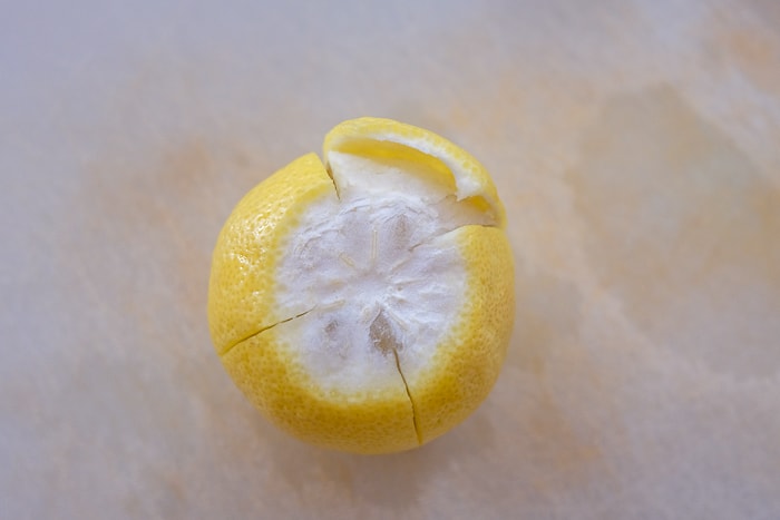 lemon with peel cut into quarters on cutting board