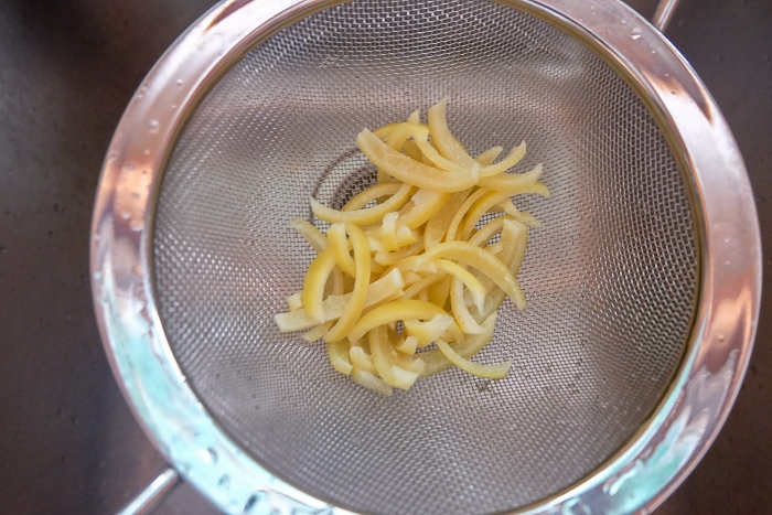 lemon peels getting rinsed in metal strainer over sink