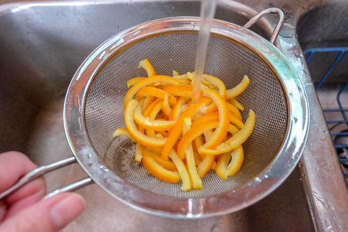 rinsing boiled orange peels in strainer in sink