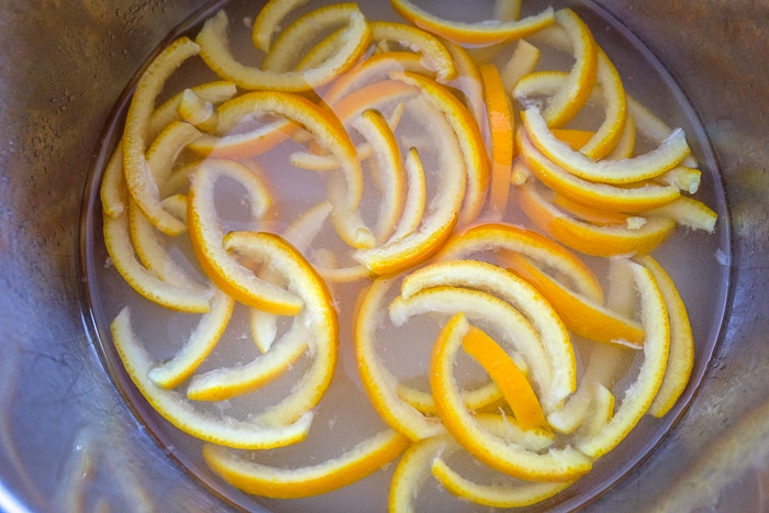sliced orange peels in sugar water in pot on stove