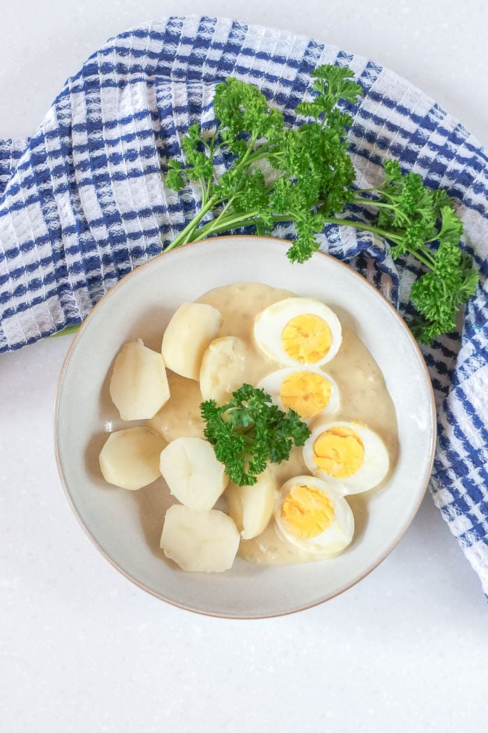 german eggs in mustard sauce with a dish towel and parsley behind