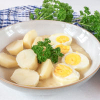 eggs in yellow mustard sauce in bowl with parsley and blue cloth behind
