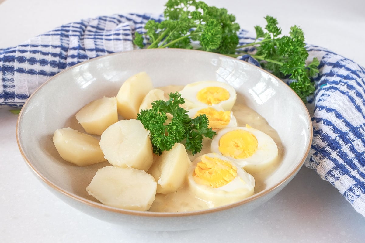 eggs in yellow mustard sauce in bowl with parsley and blue cloth behind