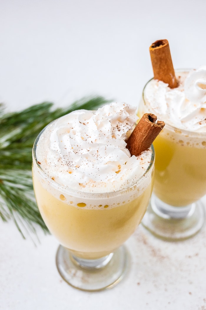 german egg punch in glasses with whopping cream and cinnamon sticks