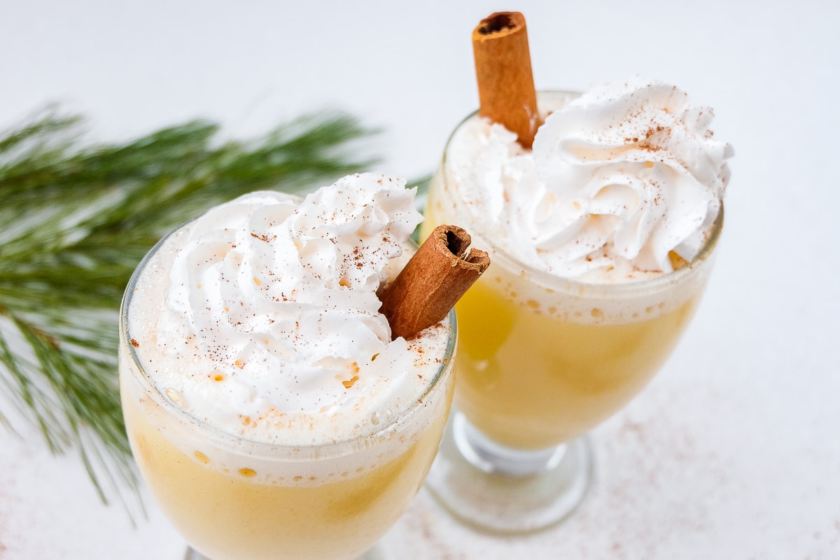 two glasses of german eierpunsch with cinnamon sticks on white counter