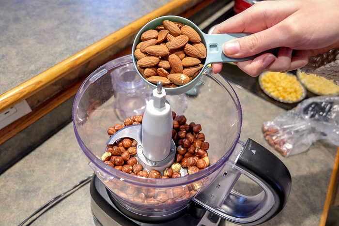 measuring cup of whole almonds pouring into food processor