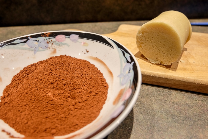 roll of marzipan on wooden board with bowl of cocoa powder beside