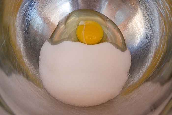 egg cracked into mixing bowl with sugar