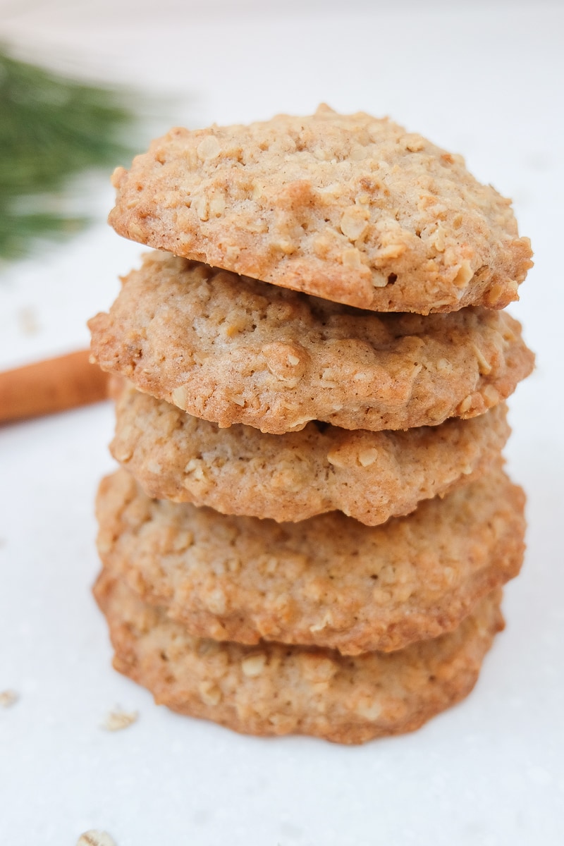 oatmeal cookies stacked on white marble board with oats and cinnamon sticks around