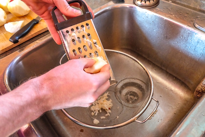 grating apples into strainer in sink