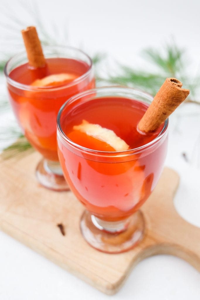 two glasses of red kinderpunsch on wooden board with cinnamon sticks