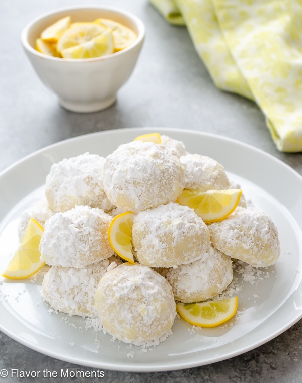 round cookies with icing sugar on top on white plate with lemon wedges as garnish.