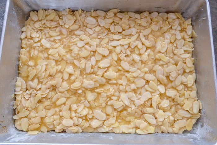 uncooked Bienenstich cake with sliced almonds on top in baking tray