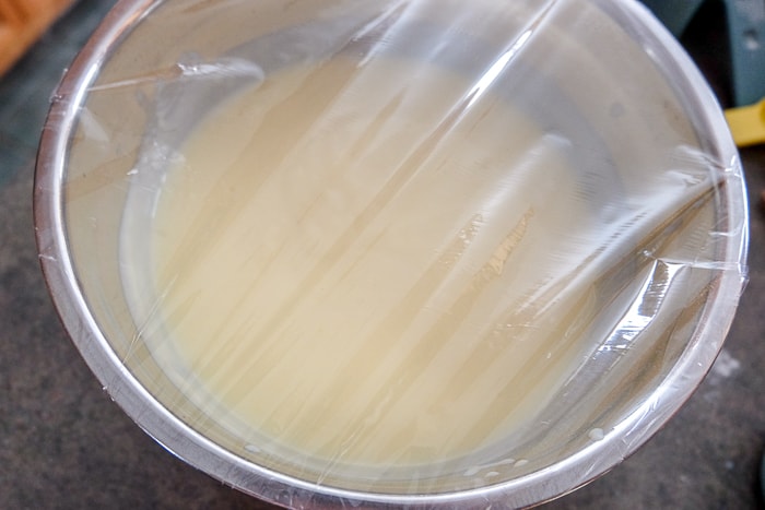 cling wrap on a mixing bowl with vanilla pudding in it