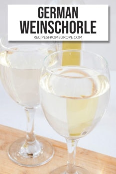 Photo of two glasses with white wine on wooden board with bottle in background and text overlay saying German Weinschorle