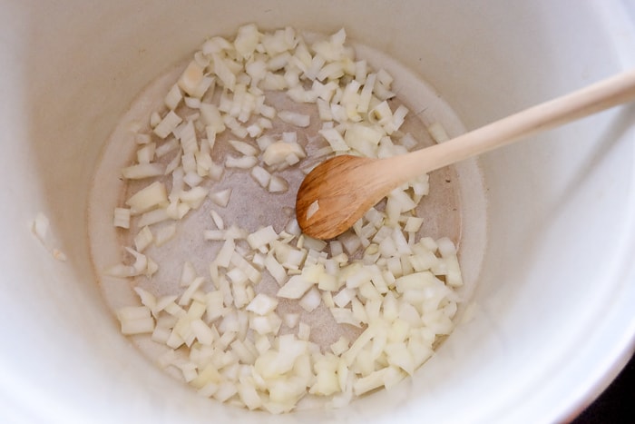 chopped onions in pot stirred with wooden spoon
