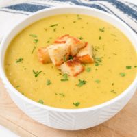 bowl of yellow creamy potato soup with croutons on top on wooden board