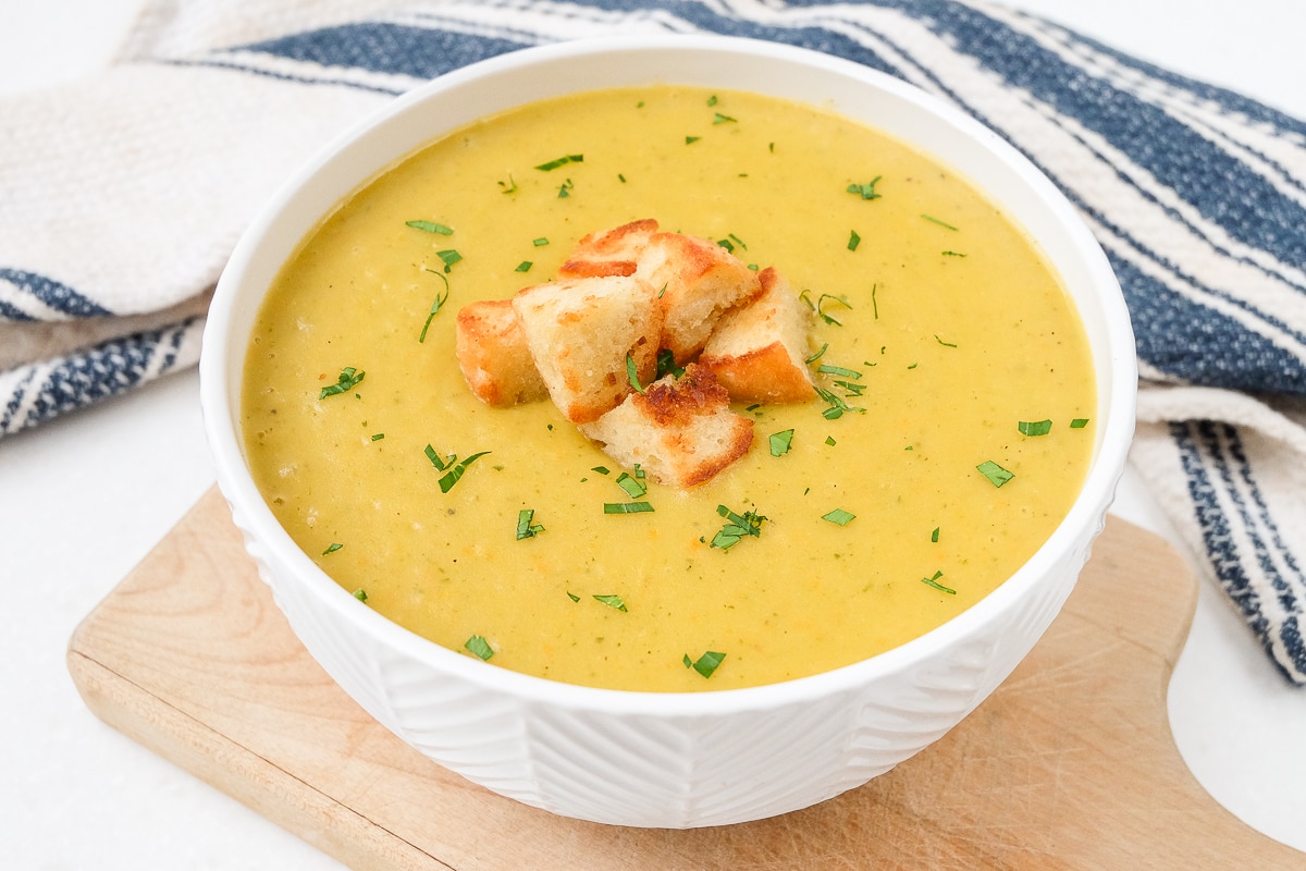 bowl of yellow creamy potato soup with croutons on top on wooden board