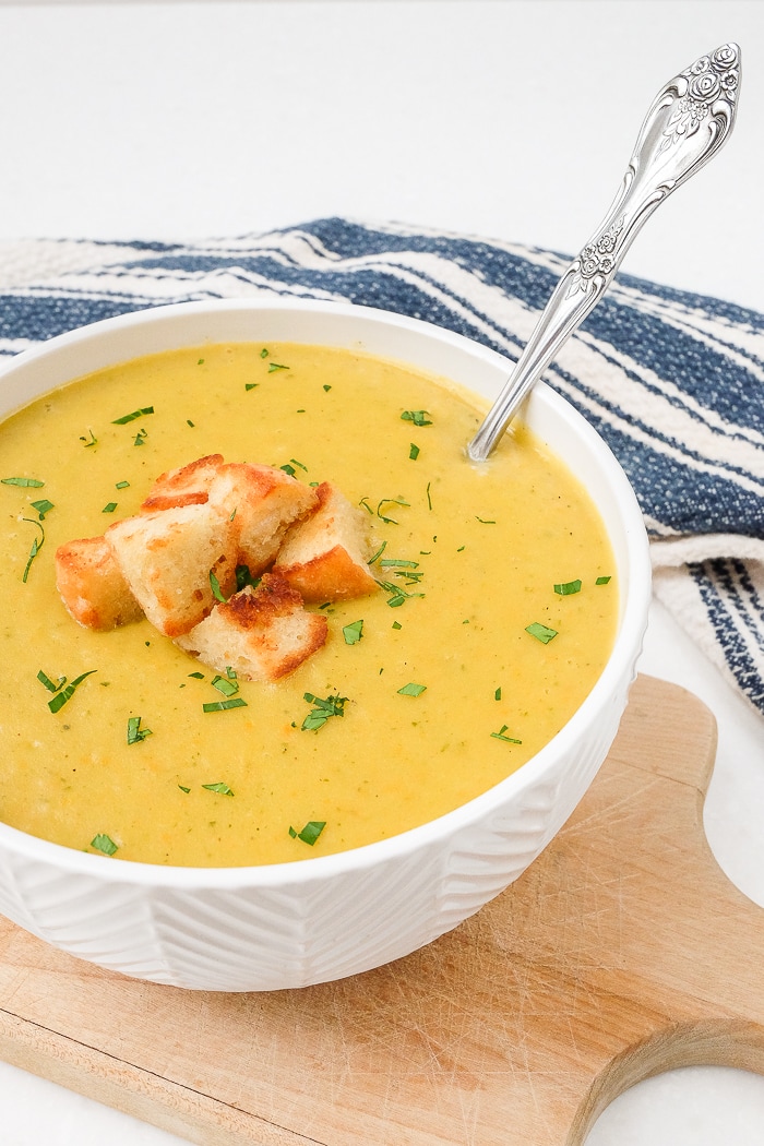creamy yellow potato soup with spoon in bowl on wooden cutting board