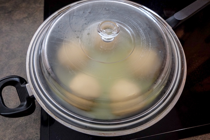 five dumplings under glass lid in black pan on stove top