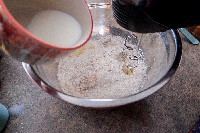 mug of milk pouring into silver bowl with dampfnudeln dough and hand mixer