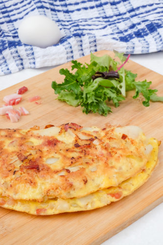 farmers omelette on wooden cutting board with egg and ham behind