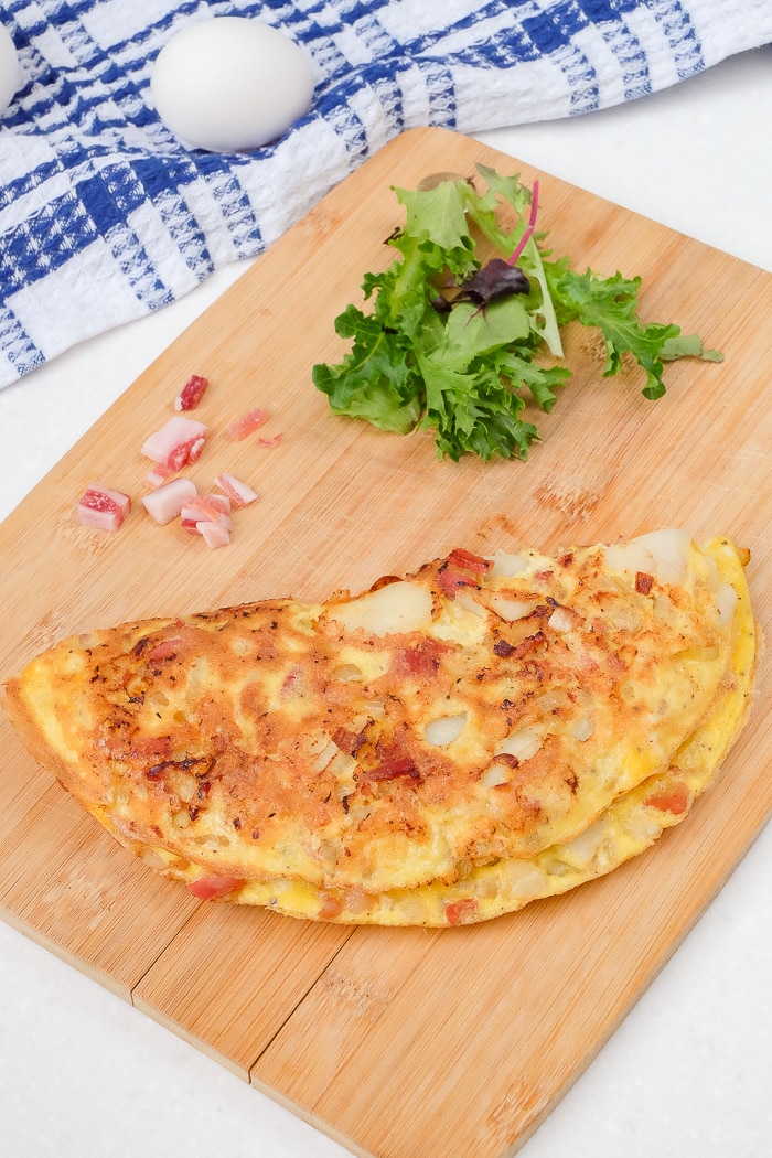 farmer's omelette on wooden cutting board with greens and egg beside