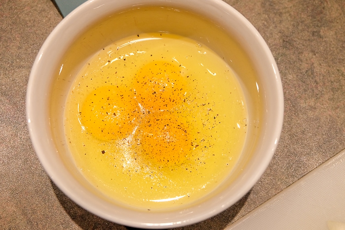 three eggs cracked into white bowl with salt and pepper