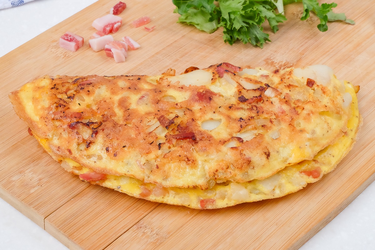 farmer's omelette on wooden cutting board with ham and greens behind