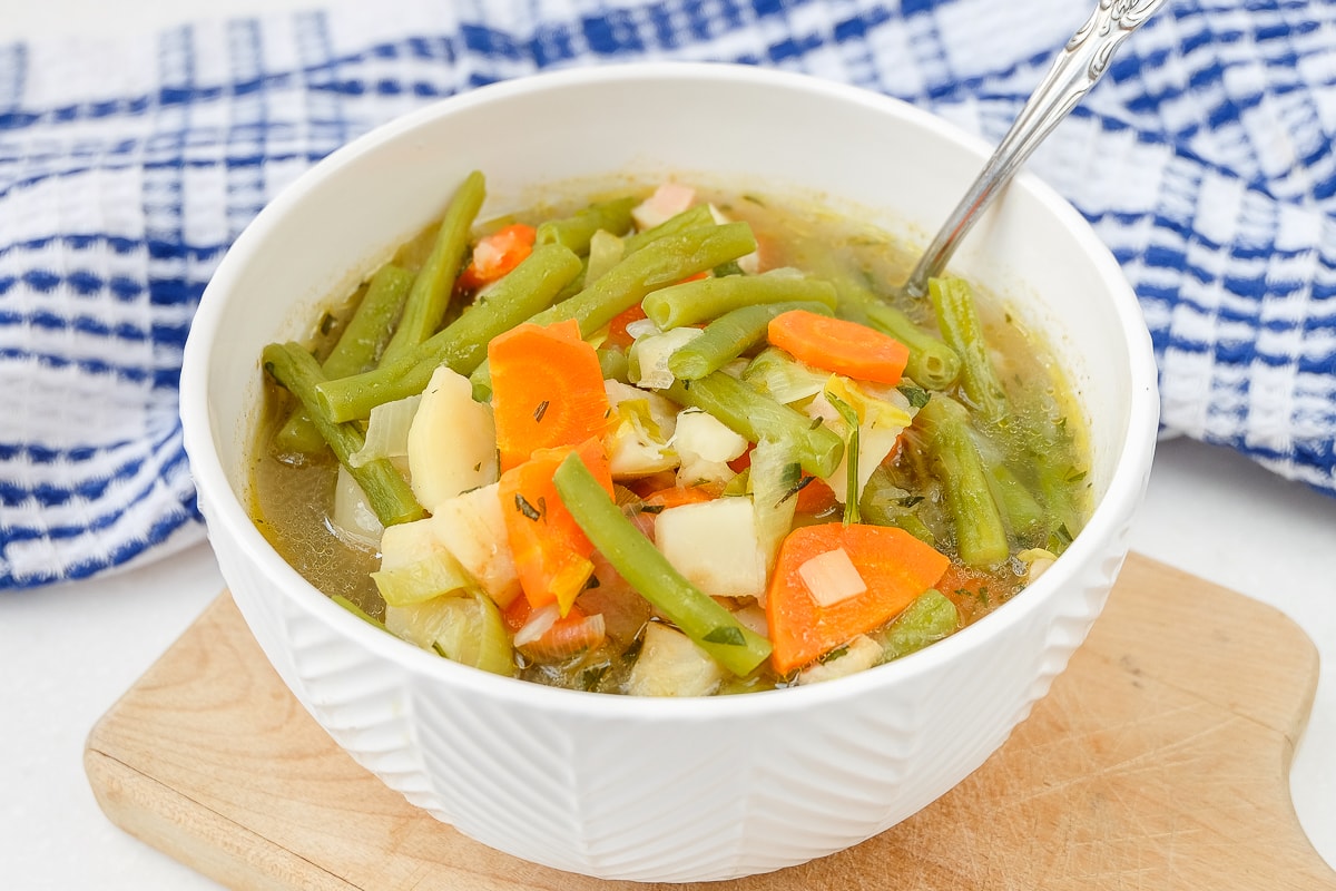 german green bean soup in white bowl with spoon sitting on wooden board