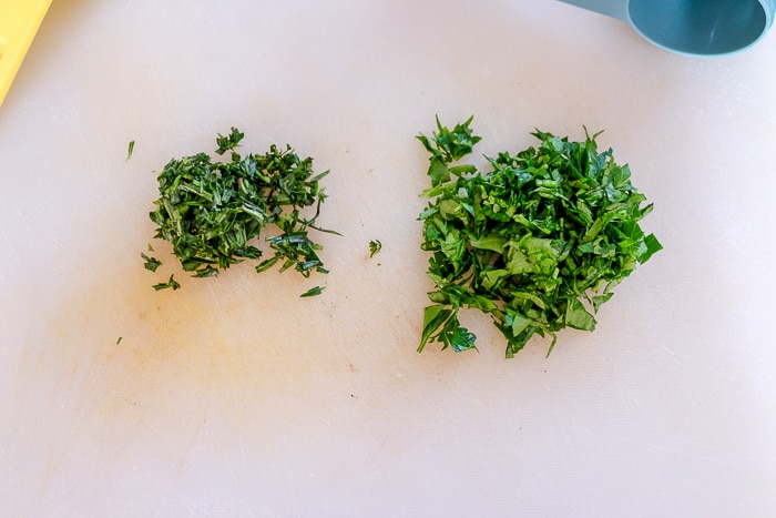 chopped parsley and savory on white cutting board in piles