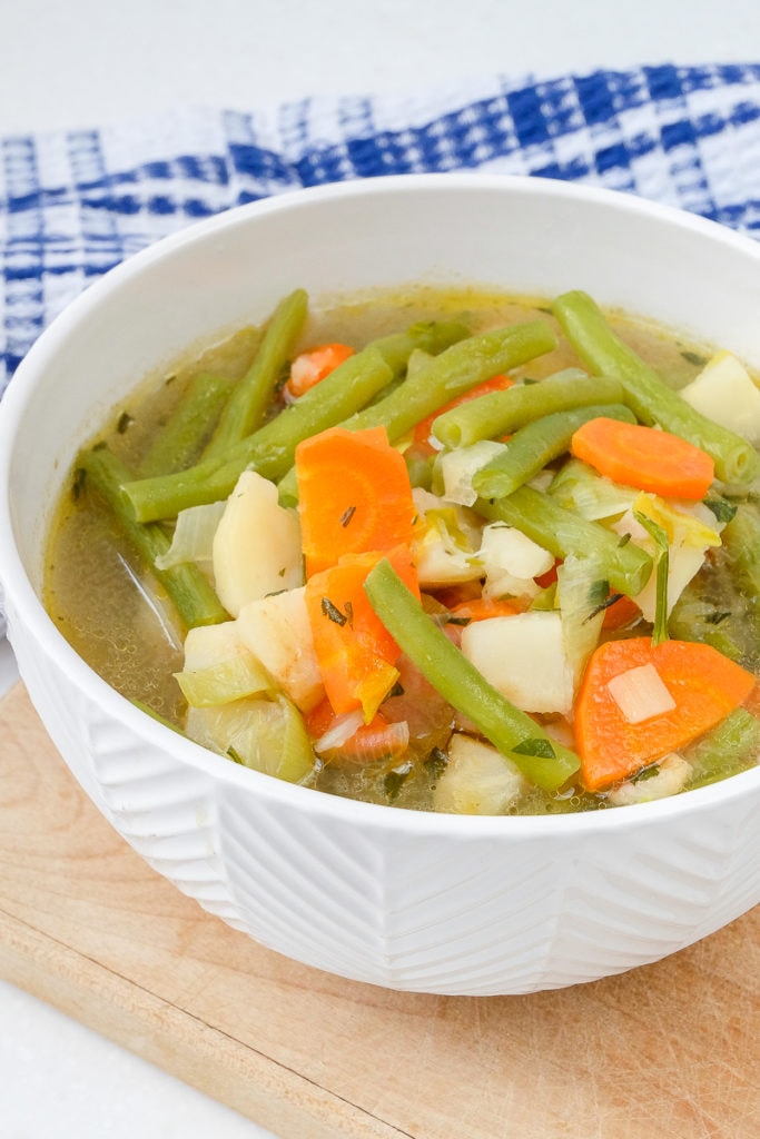 german green bean soup with vegetables in white bowl on wooden board