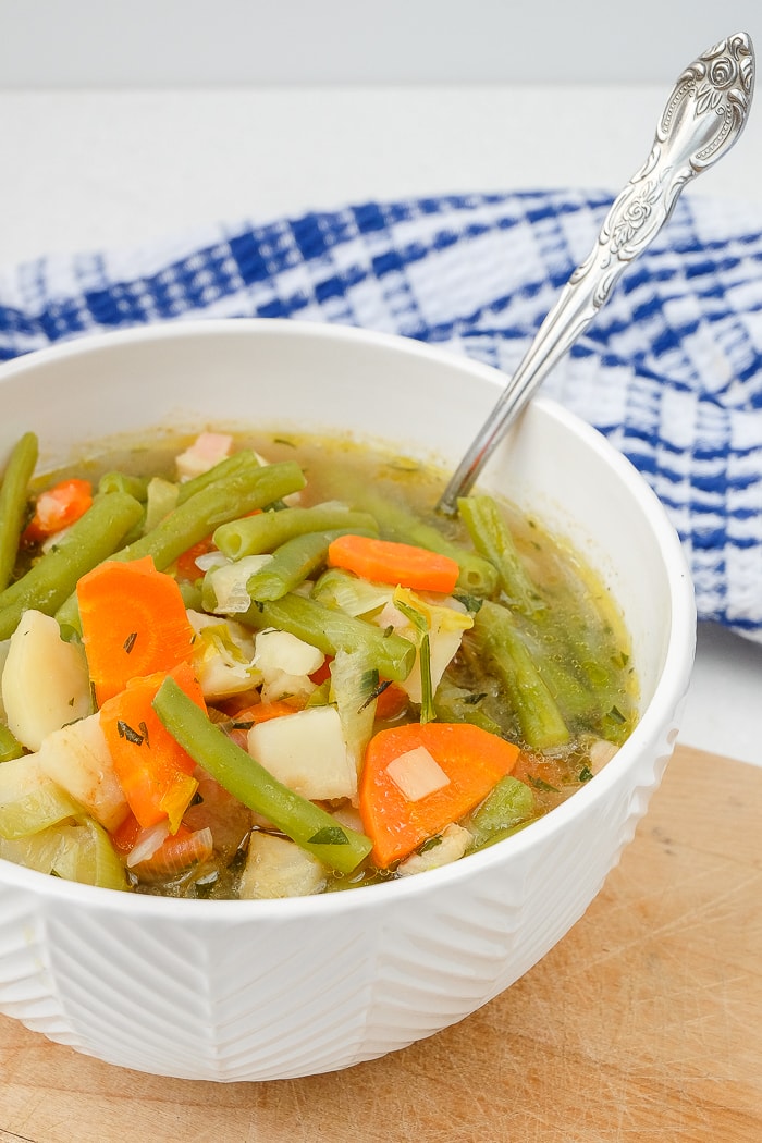 german green bean soup in white bowl with silver spoon on wooden board