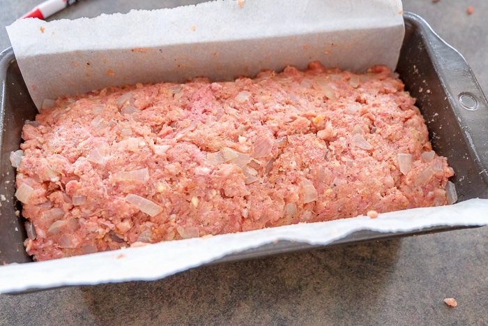 raw german meatloaf in loaf pan with parchment paper around