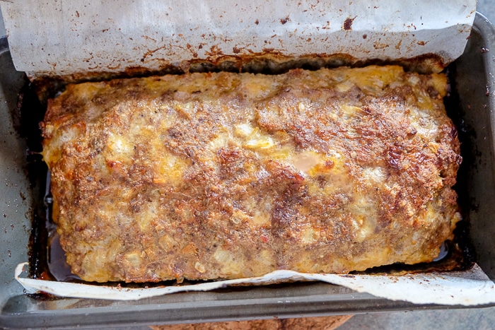 baked meatloaf in loaf pan with parchment paper around
