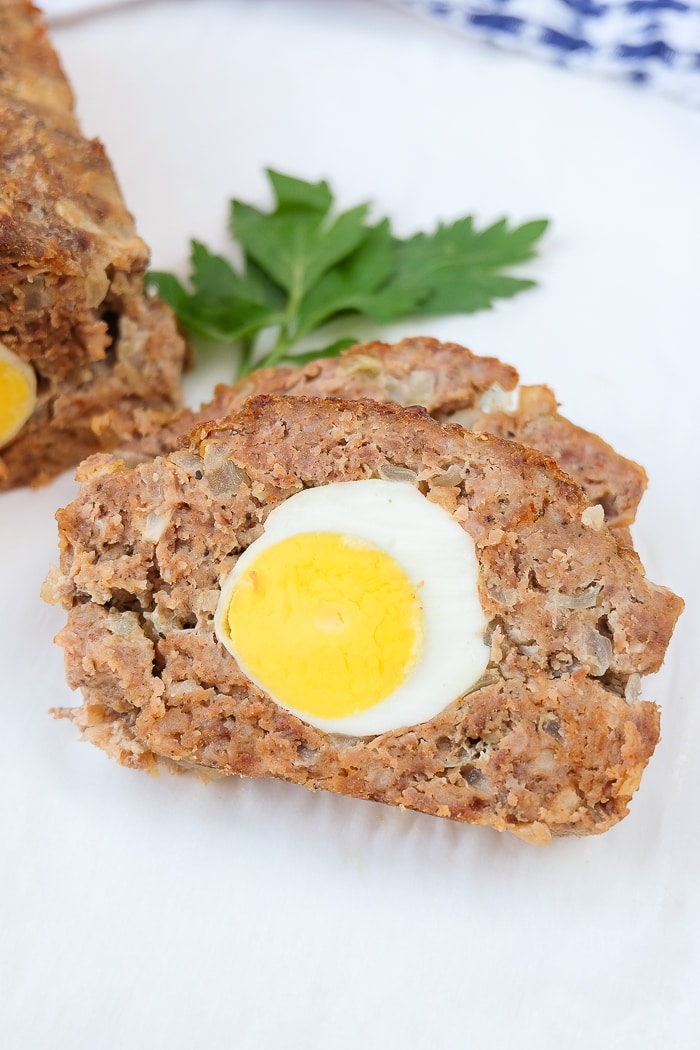 german meatloaf slice with hard boiled egg inside on plate with parsley behind
