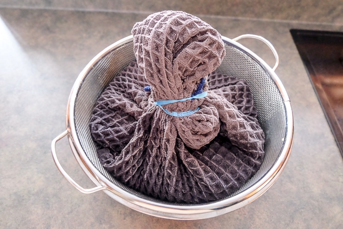 dish towel filled with quark tied up with elastic band in strainer