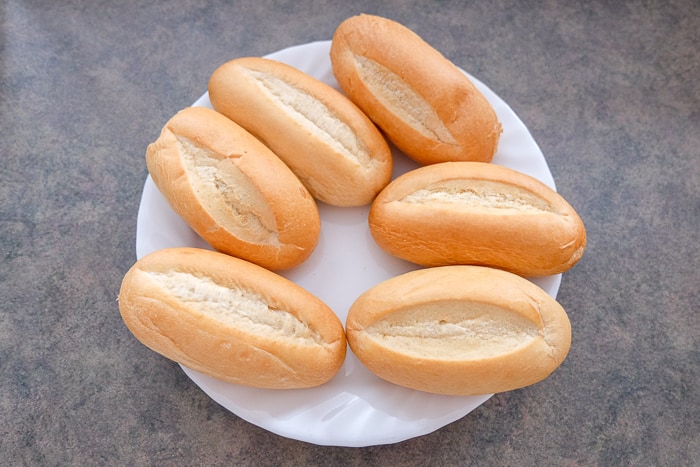six dinner rolls on white plate on counter