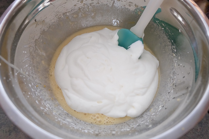 mixing whipping cream into cheesecake batter in bowl with spatula