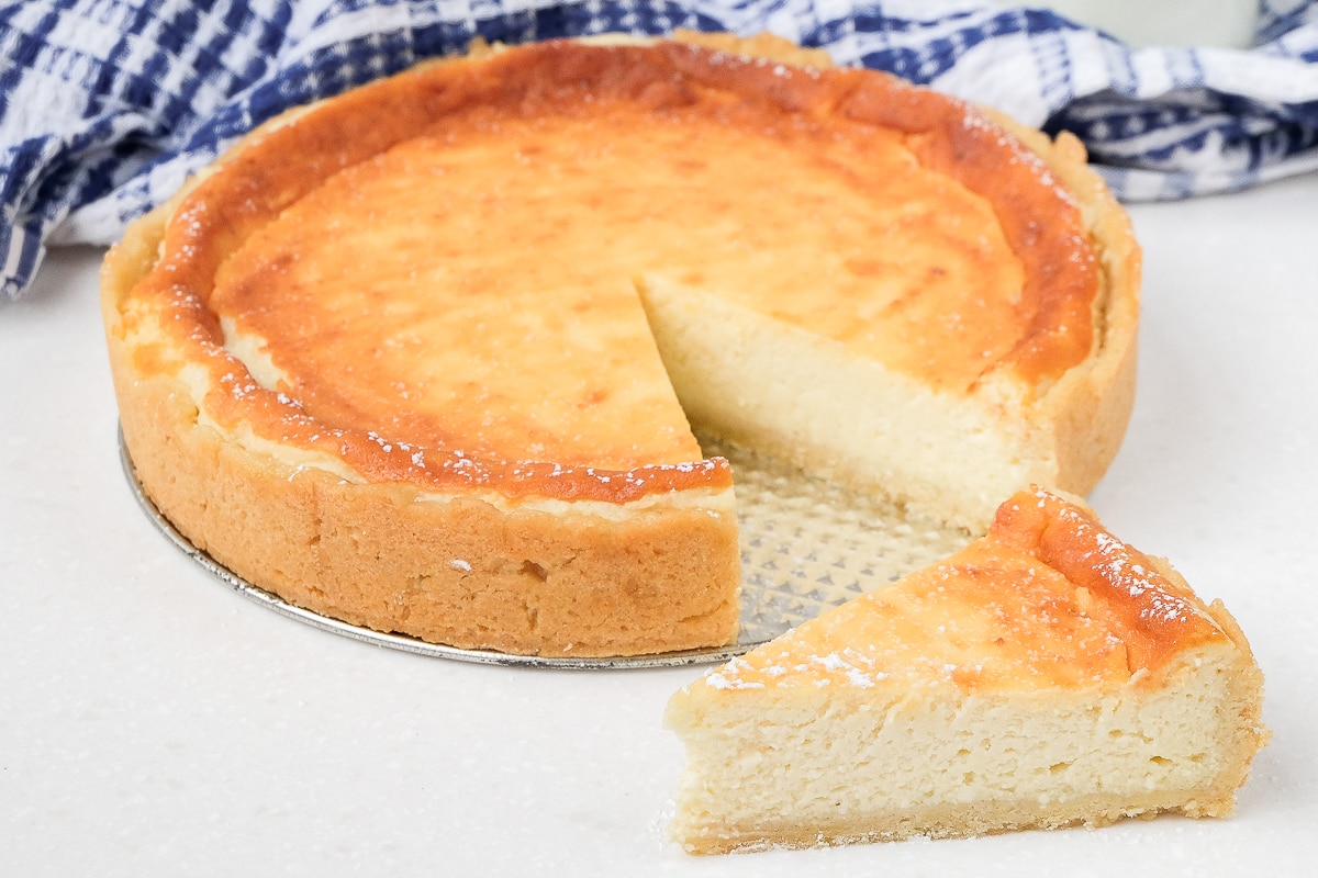 golden german cheesecake with slice cut out and displayed in front on white counter