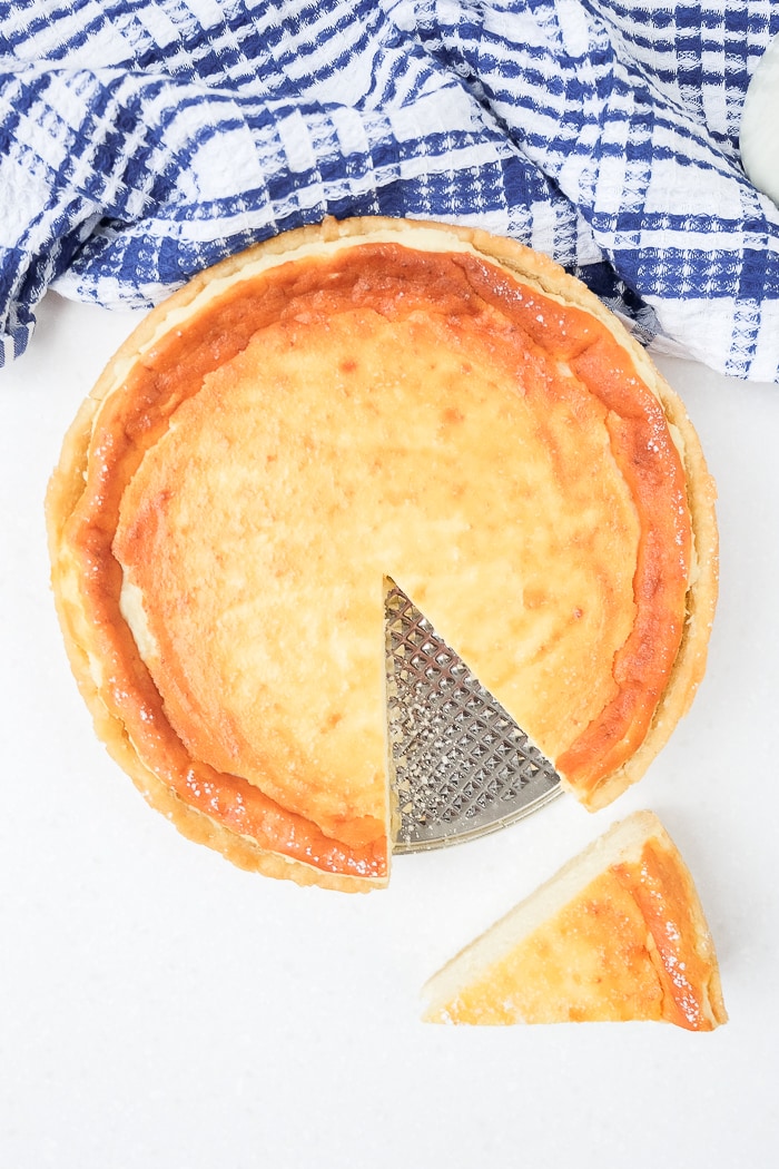german cheesecake on silver pan from above with slice cut and blue towel behind
