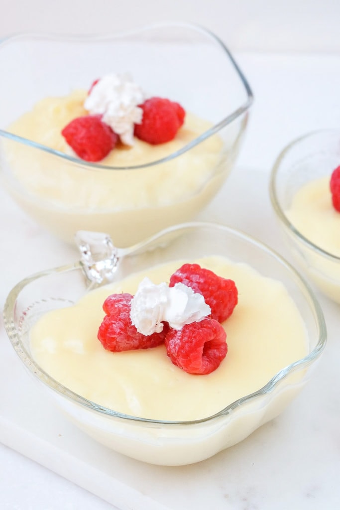 bowls of homemade vanilla pudding on white marble with raspberries on top