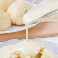 pouring vanilla sauce on german dampfnudeln with dumplings behind