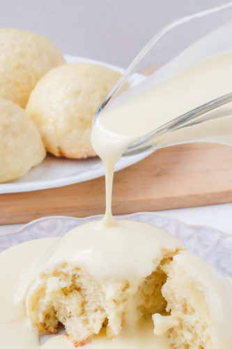 pouring vanilla sauce on german dampfnudeln with dumplings behind