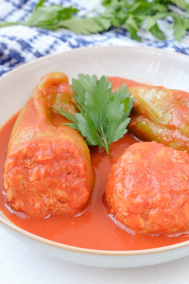 hungarian stuffed peppers in red sauce in white bowl with parsley