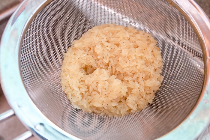 rice being rinsed in silver strainer in sink