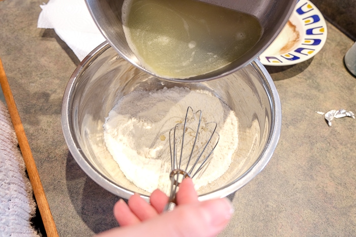 water in bowl pouring into flour with whisk in bowl