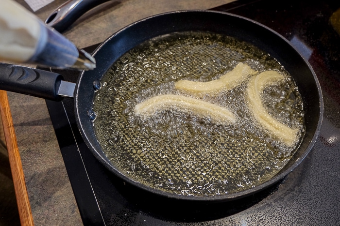 churros dough piping into frying pan of oil on stovetop